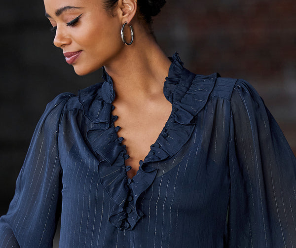 Model wearing a navy ruffle long-sleeve silver striped shirt.