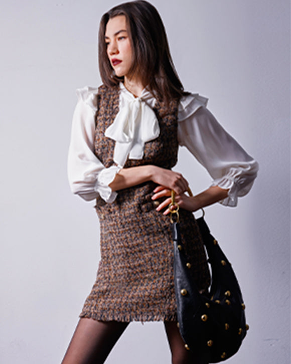 Woman wearing a white blouse and brown patterned skirt with a black handbag on a light gray background