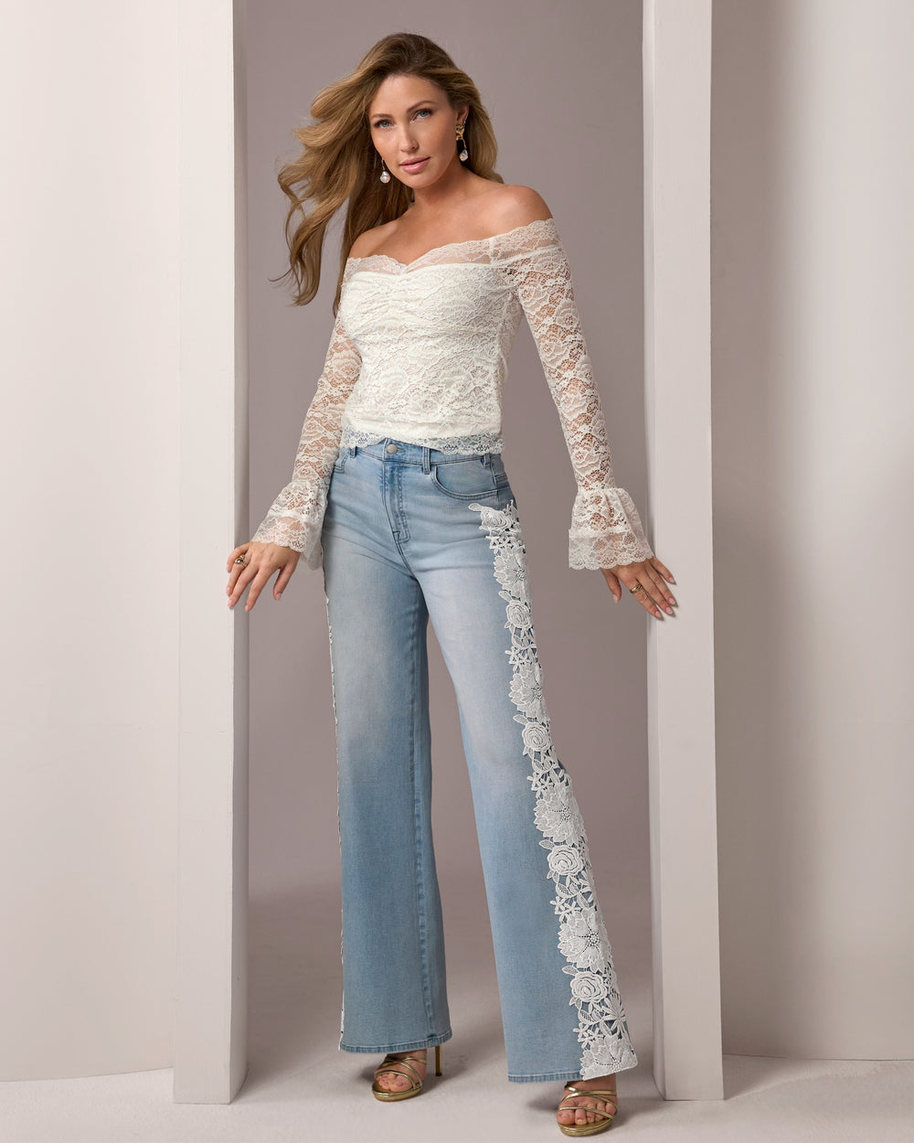 Woman wearing a white lace top and light blue jeans against a neutral background