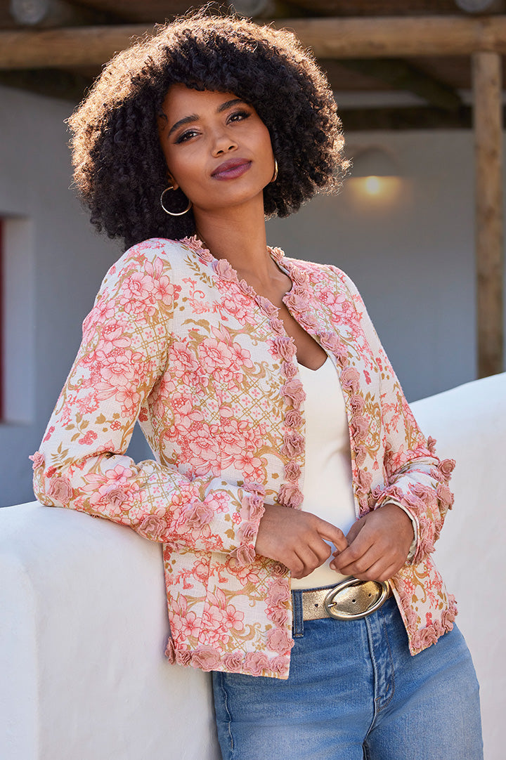 model wearing a multicolor 3d status print floral jacket, white v-neck top, gold belt, gold hoop earrings, and jeans.