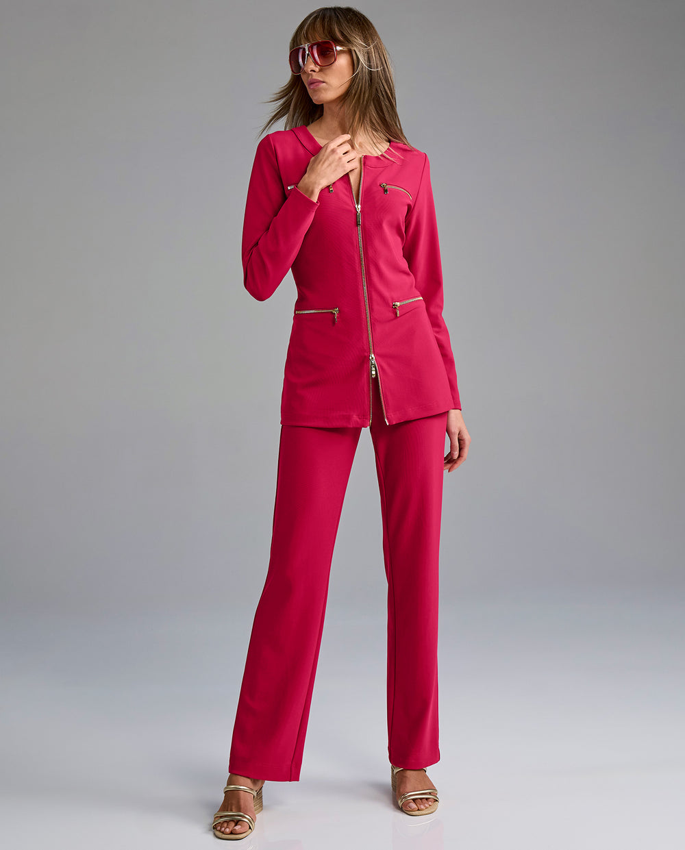 Woman wearing a pink outfit with sunglasses on a gray background