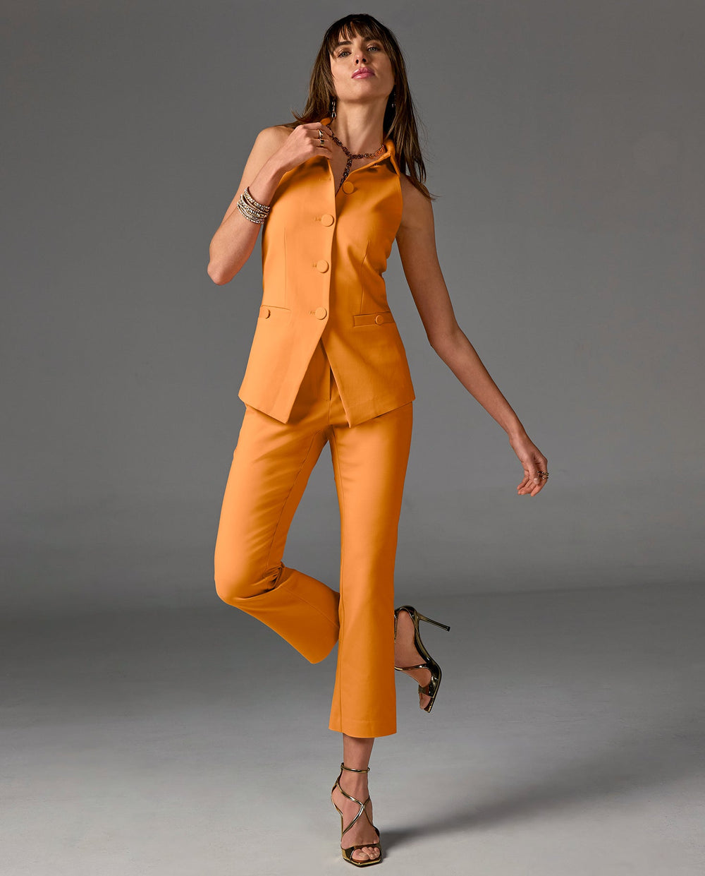 Model is wearing an orange vest top with matching pants and silver heels