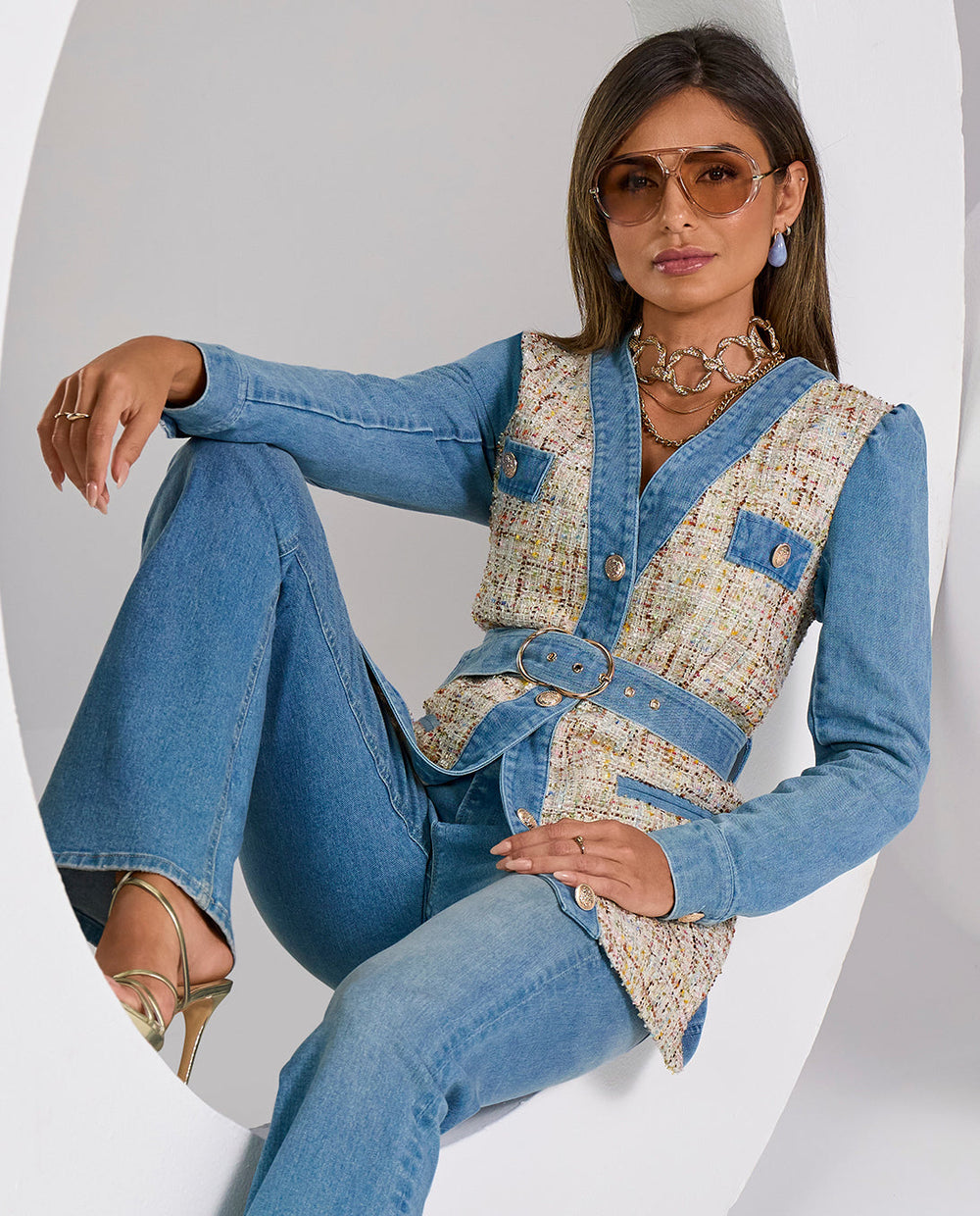 Woman wearing a denim outfit with a patterned vest against a white background