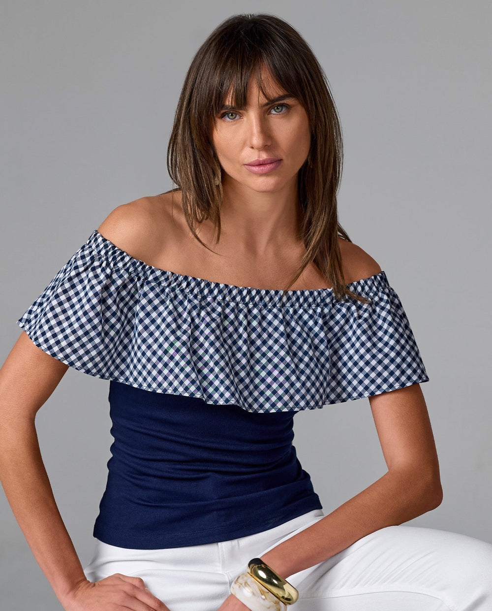 Model is wearing off the shoulder gingham top, white pants and gold bangles.