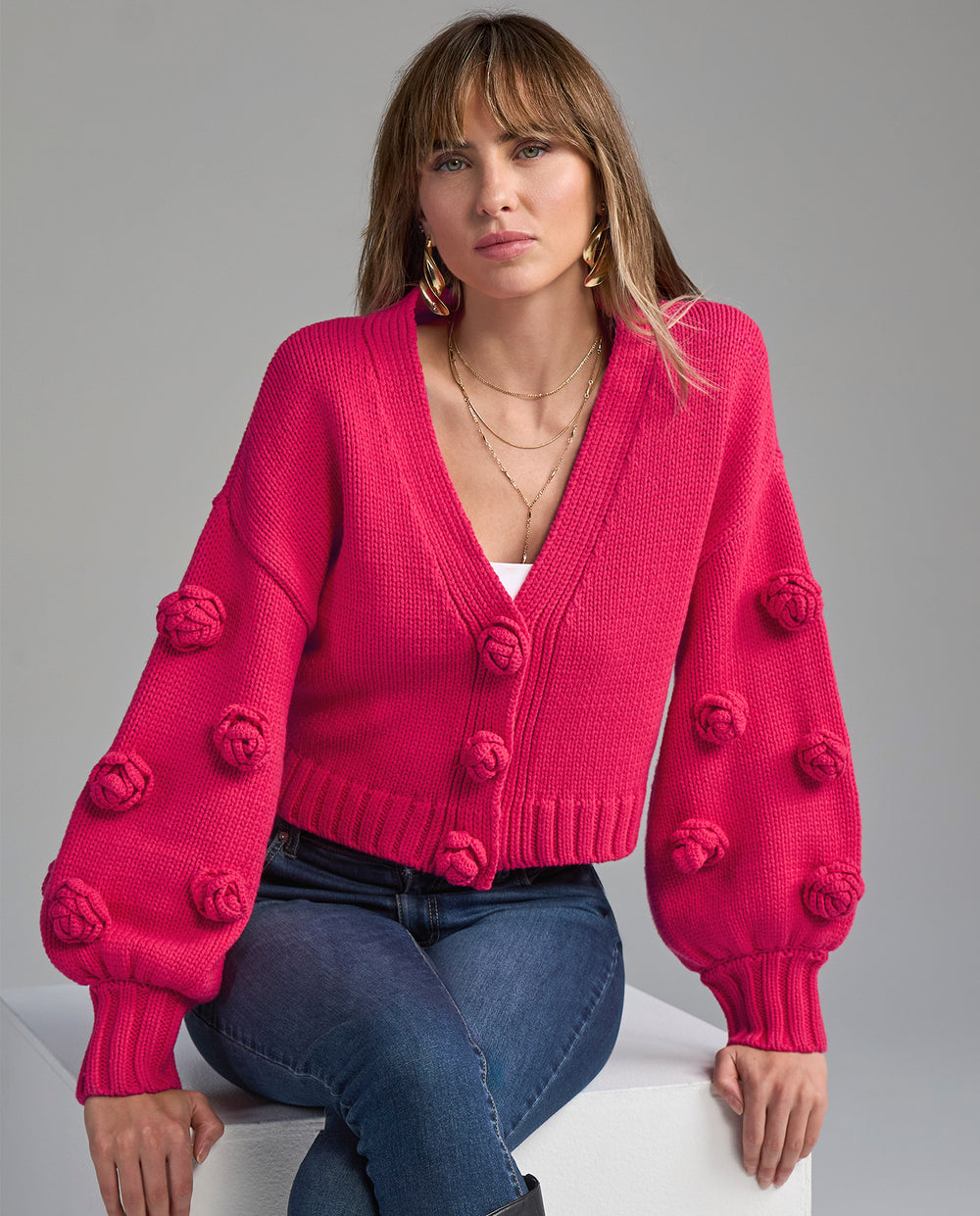 Woman wearing a bright pink sweater with pom-pom details on a gray background