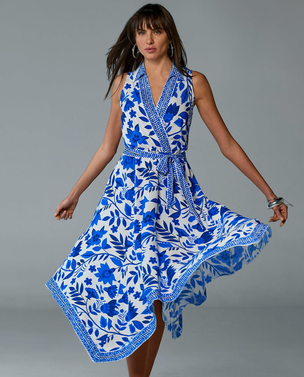 Model is wearing white and blue collared v-neck asymmetrical dress with wrap belt