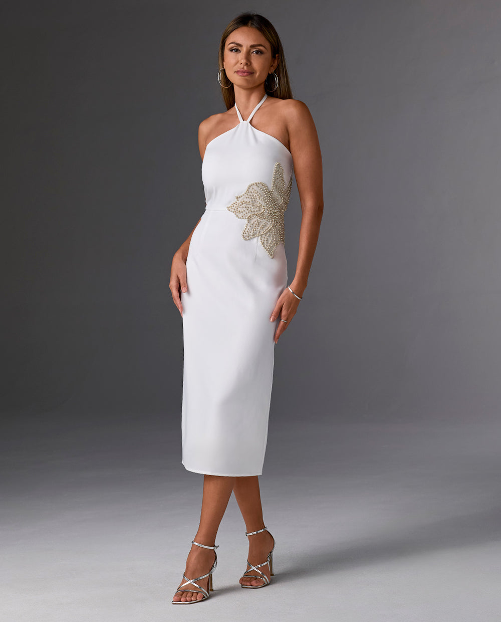 Model is wearing halter white midi dress with silver heels
