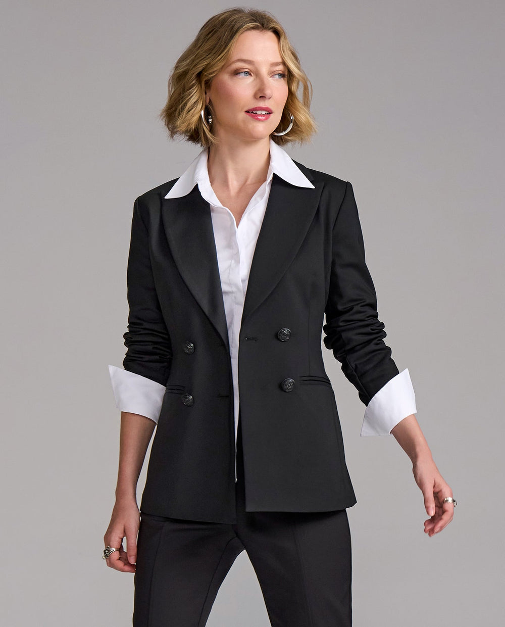 Woman wearing a black suit jacket over a white shirt on a gray background