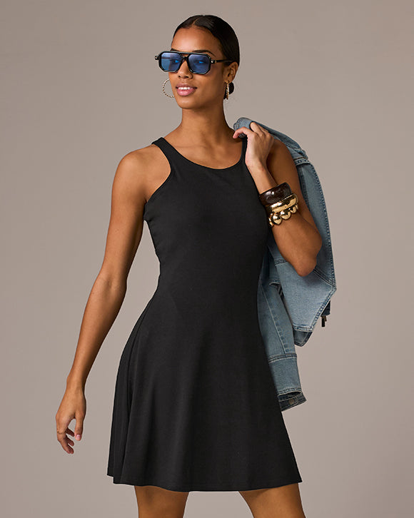 Woman wearing a black dress with sunglasses and a denim jacket on a beige background