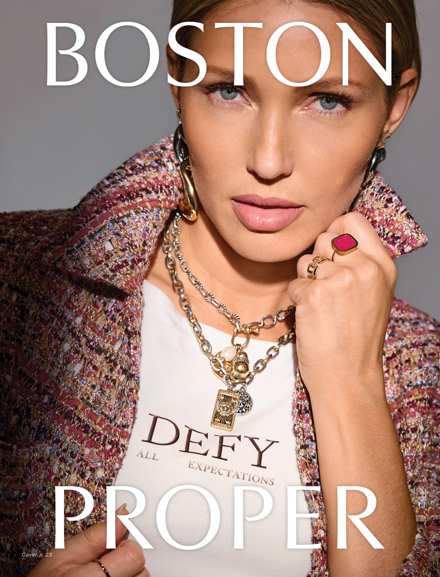 A close-up fashion portrait of a woman wearing a multicolor tweed jacket over a white graphic T-shirt, with layered gold chain necklaces and rings, against a gray studio background. Large white text reads 'BOSTON' at the top and 'PROPER' at the bottom.