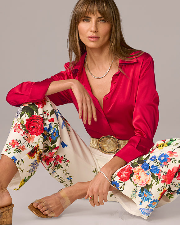 Woman wearing a red blouse and floral pants sitting on a gray background