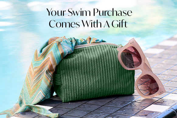 Green ribbed clutch, patterned towel, and sunglasses on a poolside surface with text 'Your Swim Purchase Comes With A Gift'.