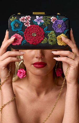 Model holding mutli color floral clutch with statement gold and pink floral earrings.