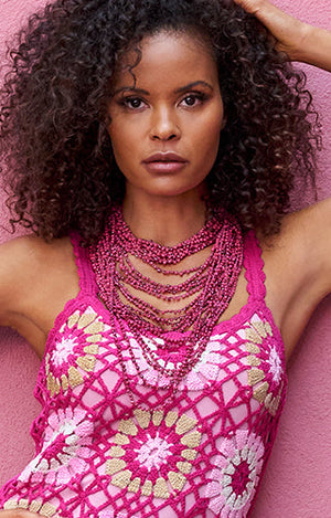 Models wearing a crochet pink dress with a long layered pink beaded necklace.