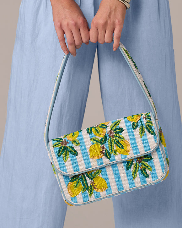 Handbag with lemon pattern held by a person wearing a blue dress.