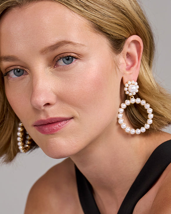 Close-up of a woman wearing pearl hoop earrings against a neutral background