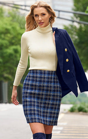 Model wearing turtleneck off white sweater, plaid mutli blue skirt and she's holding a dark navy blazer.