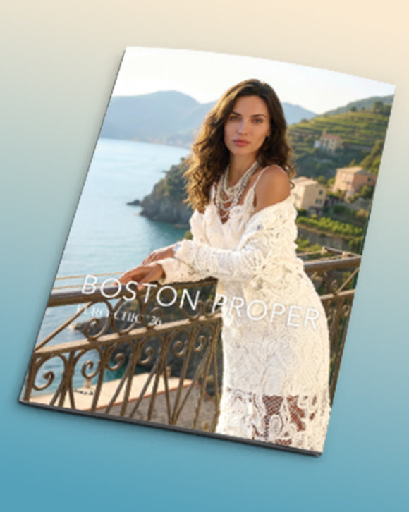 Magazine cover with a woman in a white dress sitting on a balcony overlooking a scenic landscape, featuring the brand 'Boston Proper'.