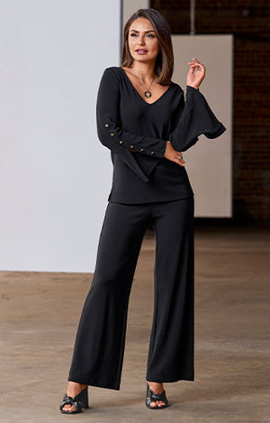 Model wearing black v neck top with gold embellishments and black Beyond Travel Palazzo Pant with heels.